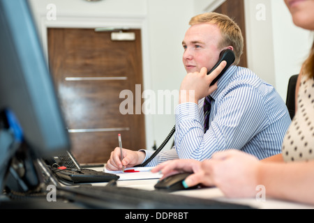 Un jeune employé de bureau se concentrer, à l'aide du téléphone et travail avec un ordinateur dans un environnement de bureau moderne Banque D'Images