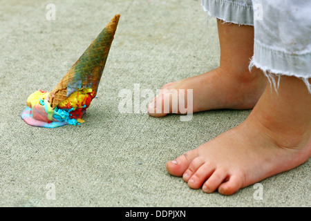 Un cornet de crème glacée de couleur arc-en-ciel met à l'envers sur le trottoir aux pieds d'un jeune enfant Banque D'Images