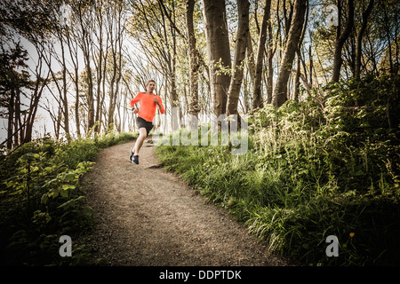 Un Yong man running sur un sentier à travers la forêt dans la région de Discovery Park, Seattle, Washington, USA. Banque D'Images