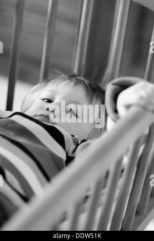 Image en noir et blanc d'un malheureux enfant couché et la maintenant sur son lit de bars. Banque D'Images