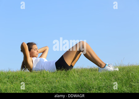 Jolie femme faisant des craquements sur l'herbe verte avec le ciel en arrière-plan Banque D'Images