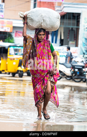 Personnes âgées femme indienne portant un sac sur sa tête sous la pluie. Puttaparthi, Andhra Pradesh, Inde Banque D'Images