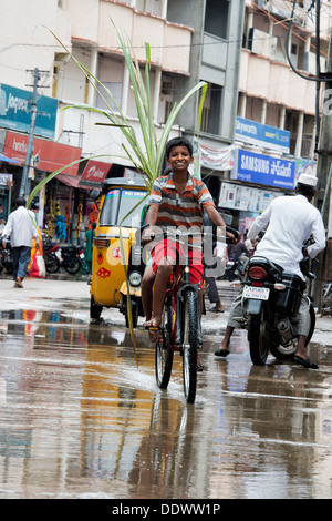 Les jeunes garçons indiens du vélo dans une flaque d'eau dans la pluie transportant la canne à sucre. Puttaparthi, Andhra Pradesh, Inde Banque D'Images