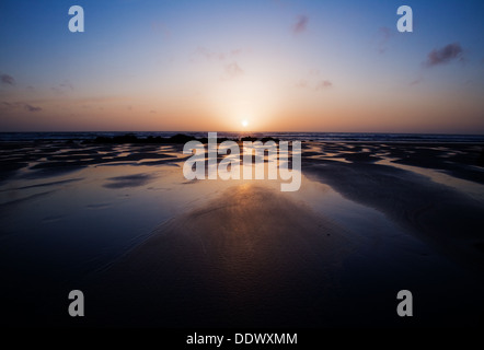 Puits de soleil derrière horizon à Porthtowan, Cornwall avec reflets colorés dans les piscines d'eau sur la plage. Banque D'Images