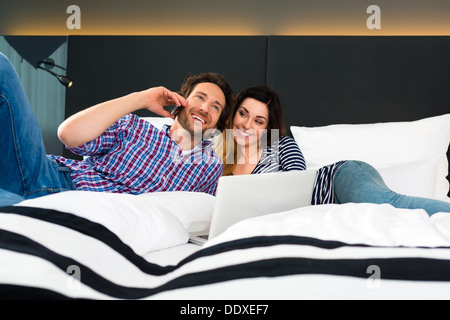 Jeune couple couché dans le lit d'une chambre d'hôtel, suite, ils sont en vacances et l'utilisation du wifi dans la chambre Banque D'Images