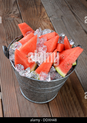 Libre d'un seau rempli de tranches de melon d'eau et de glace concassée. Le seau est assis sur une table de pique-nique en bois rustique. Banque D'Images