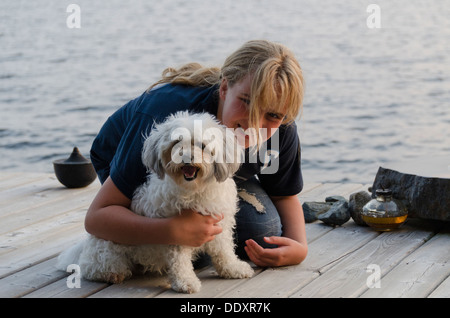 Fille sur un quai avec son animal de compagnie Zuchon chien au bord de lac, le lac des Bois, Keewatin (Ontario), Canada Banque D'Images