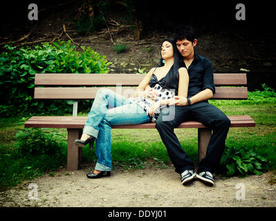 Jeune couple assis sur un banc de parc Banque D'Images