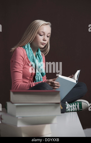 Teenage girl reading a book, avec une pile de livres à l'avant Banque D'Images