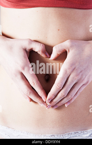 Jeune femme avec ses mains formant un coeur sur son ventre Banque D'Images