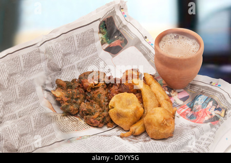 Pakoras indiens , bhajiyas et boules de pommes de terre frites avec chai en tasse traditionnelle faite de boue sur un journal Banque D'Images