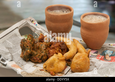 Pakoras indiens , bhajiyas et boules de pommes de terre frites avec chai en tasse traditionnelle faite de boue sur un journal Banque D'Images