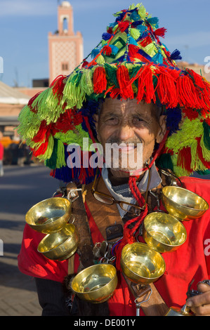 Porte-eau traditionnel habillé en rouge avec des tasses en laiton autour de son cou qui pose pour un portrait dans la place Djemaa el Fna, Marrakech, Maroc Banque D'Images