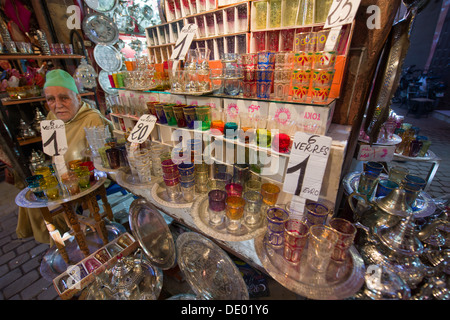 Stall keeper à l'affût des clients en face de son magasin de vente verrerie, dans le souk de Marrakech, Maroc Banque D'Images