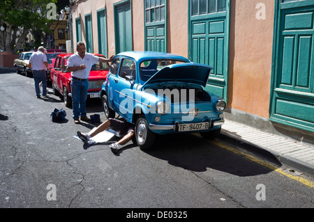 Seat 600 vintage car ventilées avec homme étendu sous les réparations exigées pendant qu'un autre regarde sur. Banque D'Images