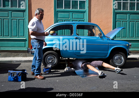 Seat 600 vintage car ventilées avec homme étendu sous les réparations exigées pendant qu'un autre regarde sur. Banque D'Images