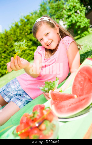 Girl eating salad, pastèque, un bol de fraises, dans un jardin Banque D'Images