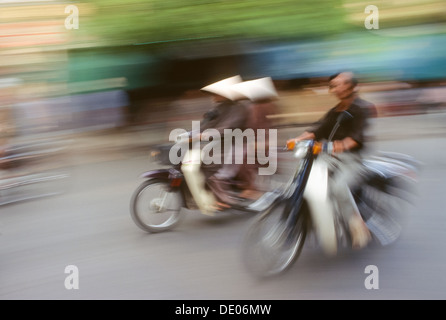 Deux femmes à chapeaux coniques sur une accélération des cyclomoteurs dans le vieux quartier de Hanoi, Vietnam Banque D'Images