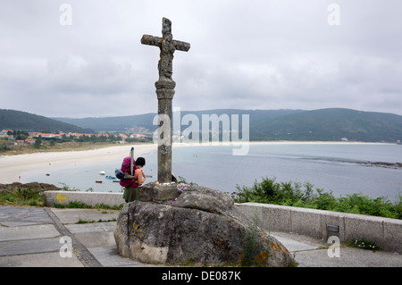 Un pèlerin montre l'une des plages de Finisterre à côté de l'une des croix en pierre du chemin de St-Jacques. Banque D'Images