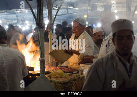Flammes fanning Cook saucisses prêtes à cuire, à un foodstall dans la place Djemaa el Fna, Marrakech, Maroc Banque D'Images