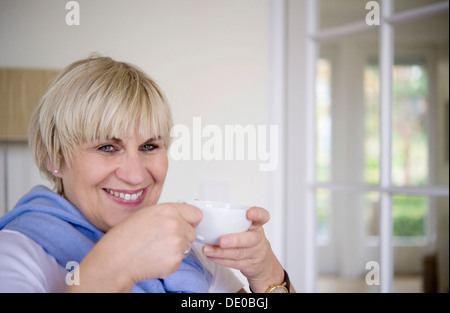 Une femme est assise et boire d'une tasse de thé dans son bureau Banque D'Images