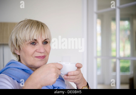 Une femme est assise et boire d'une tasse de thé dans son bureau Banque D'Images