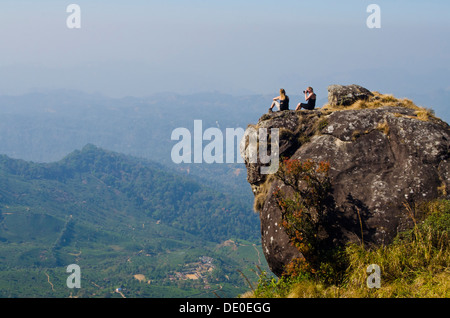 Deux personnes assis sur un gros rocher surplombant la pendaison des plantations de thé, Munnar, Inde du Sud Kerela Banque D'Images