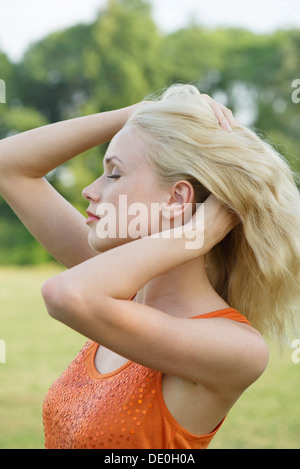 Jeune femme touseling ses cheveux outdoors, portrait Banque D'Images