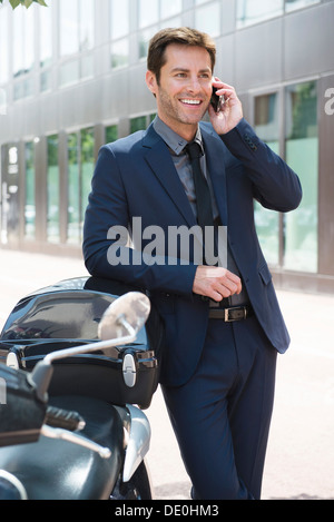 Businessman talking on cell phone in city, appuyé contre des scooters Banque D'Images