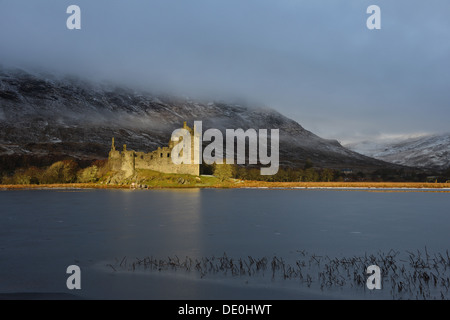 Ruines du château de Kilchurn vu derrière frozen Loch Awe illuminée par le soleil matinal. Banque D'Images