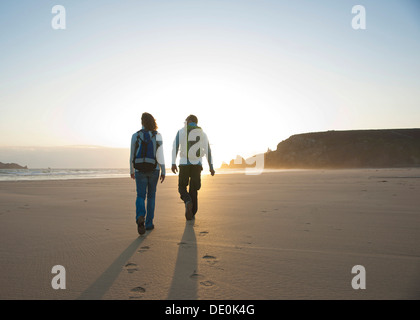 Couple en train de marcher le long de la plage vers le coucher du soleil Banque D'Images