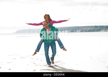 Homme portant une femme sur une plage de ferroutage Banque D'Images