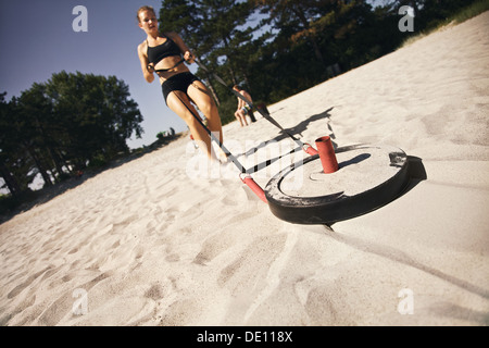 Jeune femme forte tirant un traîneau crossfit sur une plage de sable fin à l'extérieur sur une chaude journée d'été Banque D'Images