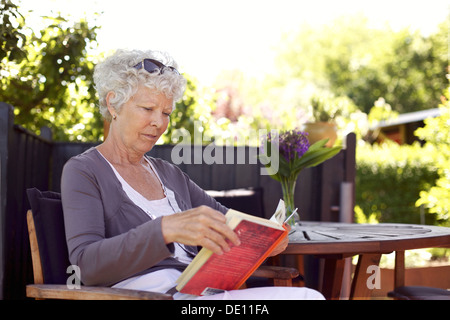Ambiance senior woman sitting une chaise dans le jardin en lisant un livre Banque D'Images