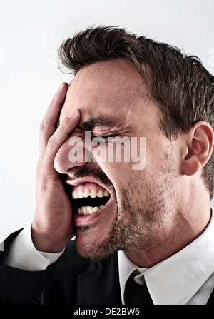 Desperate young man wearing a suit couvrant son visage avec sa main, de crier Banque D'Images