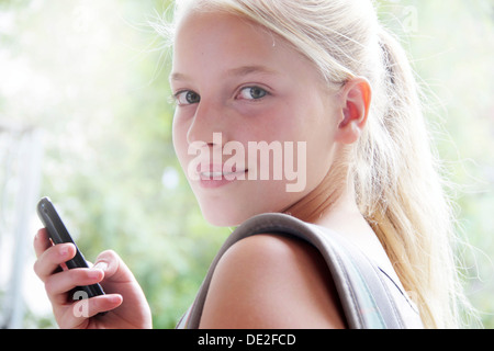 Jeune fille à la recherche vers la caméra et la tenue d'un smartphone dans la main Banque D'Images