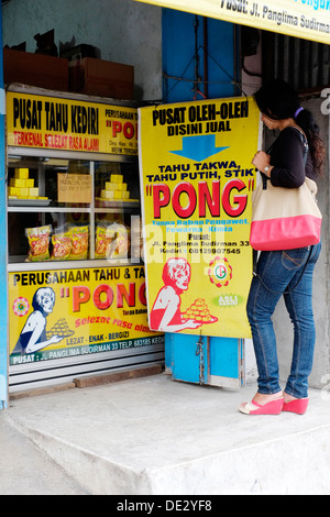 Femme debout par magasin de vente local le tofu avec le nom de marque de commerce de pong medan indonésie java Banque D'Images