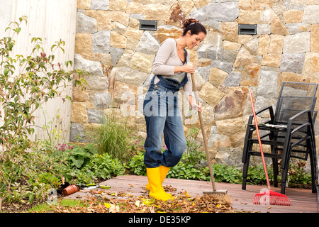 Jeune femme balayant les feuilles d'automne jardin véranda tas de nettoyage Banque D'Images