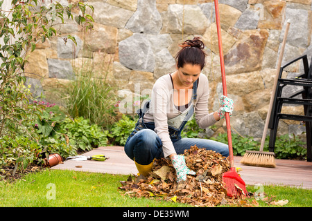 Jeune femme ramasser des feuilles automne pile véranda du jardin ménage balayant Banque D'Images