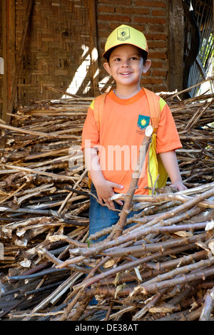 Heureux petit garçon dans son uniforme scolaire l'article parmi un tas de couper des bâtonnets de bois Banque D'Images