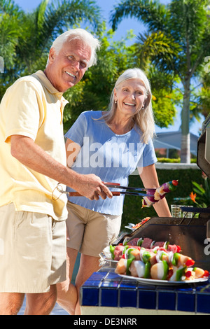 Happy senior man and woman couple en dehors de la cuisson brochettes sur le barbecue d'été Banque D'Images