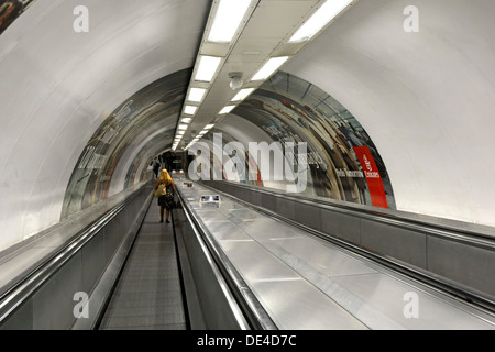 Femme seule sur un trottoir roulant dans un long tunnel bien éclairé menant à la plate-forme de train souterrain Londres Angleterre Royaume-Uni Banque D'Images