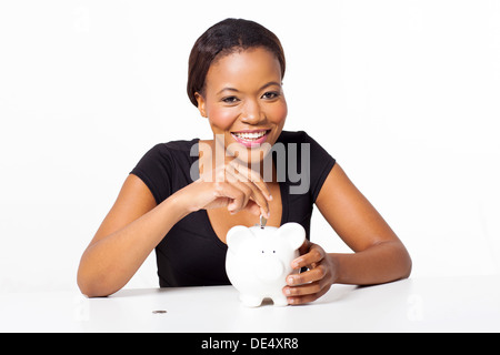 Pretty African woman putting coins in piggy bank isolated on white Banque D'Images