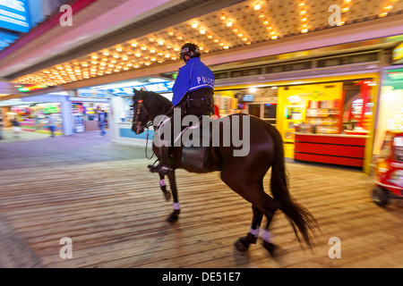 Un policier en patrouille à cheval sur un cheval déambule sur un trottoir de l'océan par les jeux de hasard et de fast food restaurants. Banque D'Images