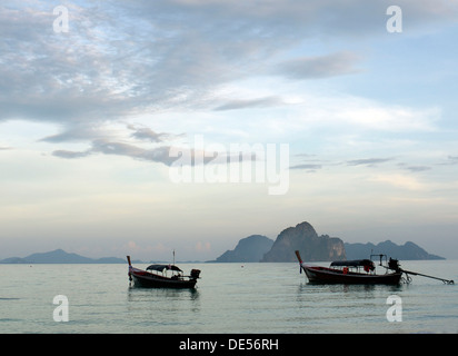 Long Tail boats vu à l'aube, dans l'arrière d'un groupe de roches et de l'île de Ko Muk, vu de la plage de Ko Hai, l'île de Ko Ngai Banque D'Images