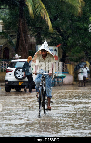 Adolescent indien du vélo à travers une route inondée avec un sac sur la tête. Puttaparthi, Andhra Pradesh, Inde Banque D'Images