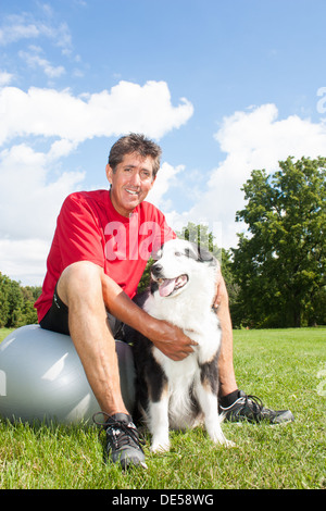 Un sourire d'un homme avec son chien heureux de prendre une pause de leur routine de remise en forme de yoga sur une journée ensoleillée dans le parc Banque D'Images