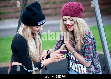 Deux adolescentes à l'extérieur à regarder leur téléphone mobile. Banque D'Images