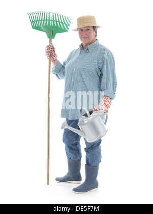 Jardinier Senior woman wearing straw hat et des bottes en caoutchouc posant avec le râteau et l'arrosoir en métal sur fond blanc Banque D'Images