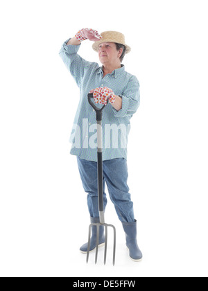 Jardinier Senior woman wearing straw hat et des bottes en caoutchouc en appui sur la fourche et à l'avant tourné sur fond blanc Banque D'Images